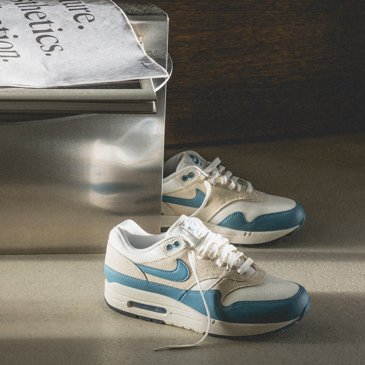 Nike Air Max 1 Soft Pearl Smokey Blue pair editorial shot with magazine showing teal leather and suede panels