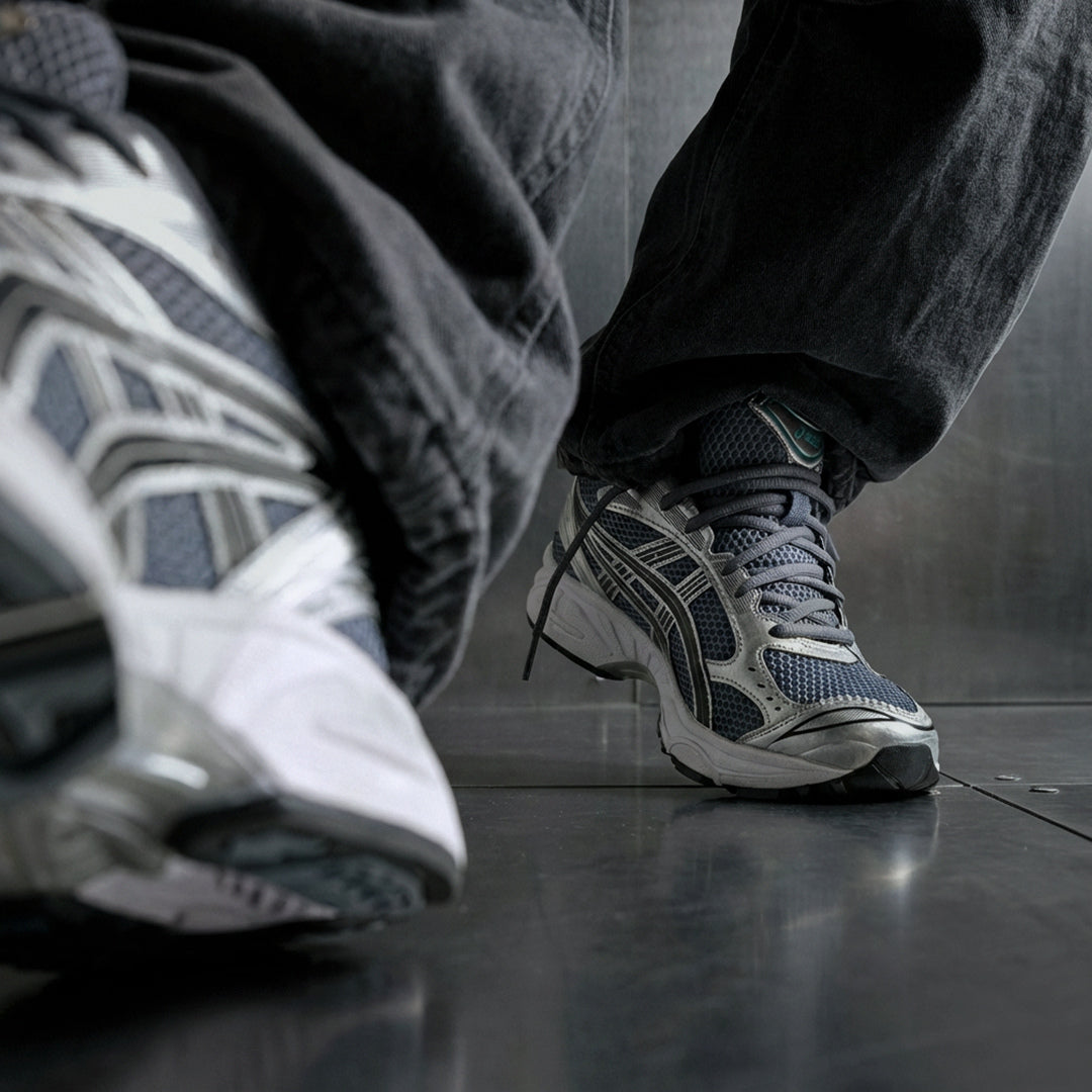 ASICS Gel-Kayano 14 Metropolis Jasper Green on foot low angle with dark denim on reflective floor showing metropolis grey mesh, silver overlays, and green GEL heel unit