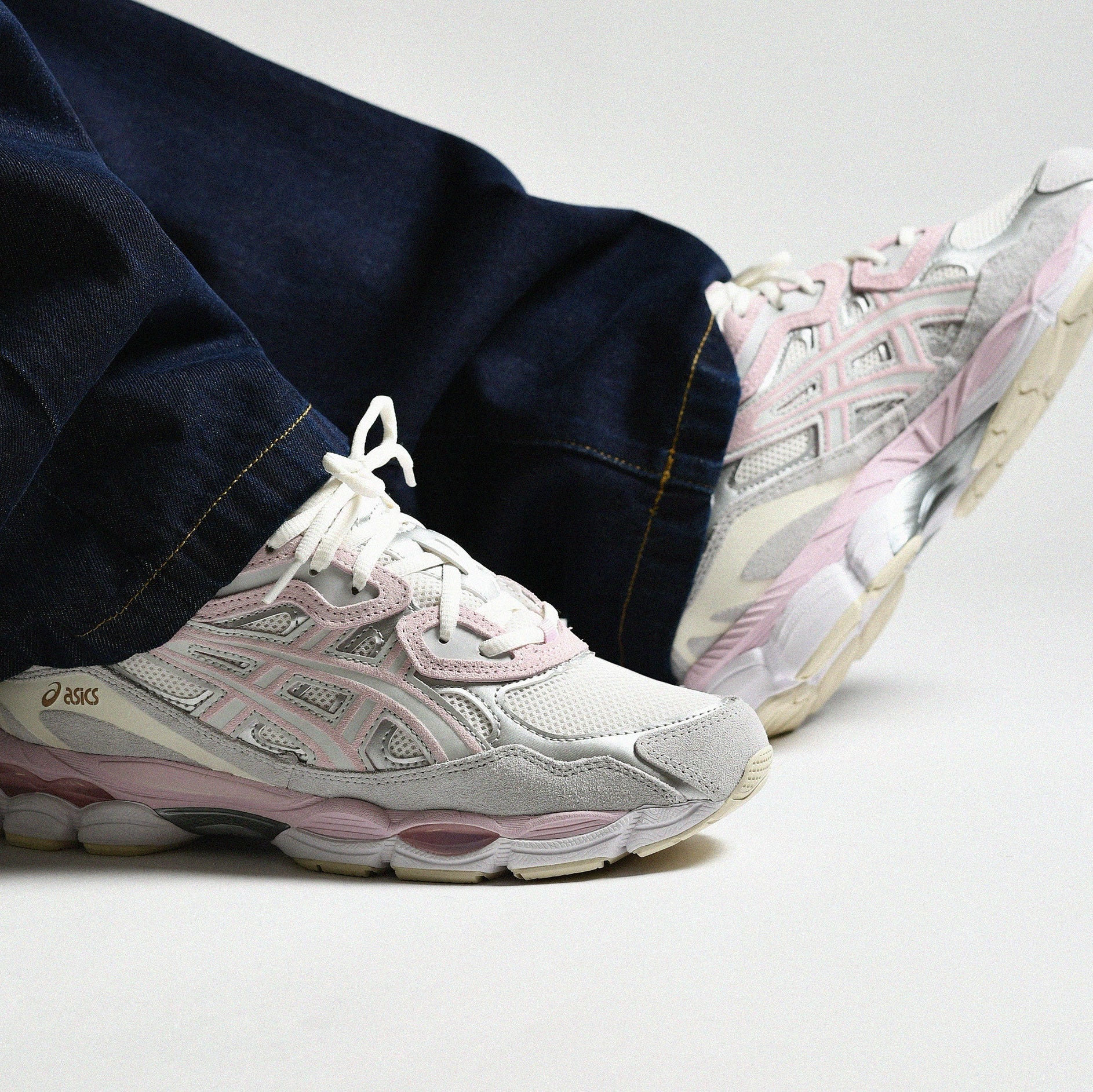 ASICS Gel-NYC Barely Rose worn on foot with dark navy denim jeans showing medial side with pink stripes, grey suede, and ASICS branding
