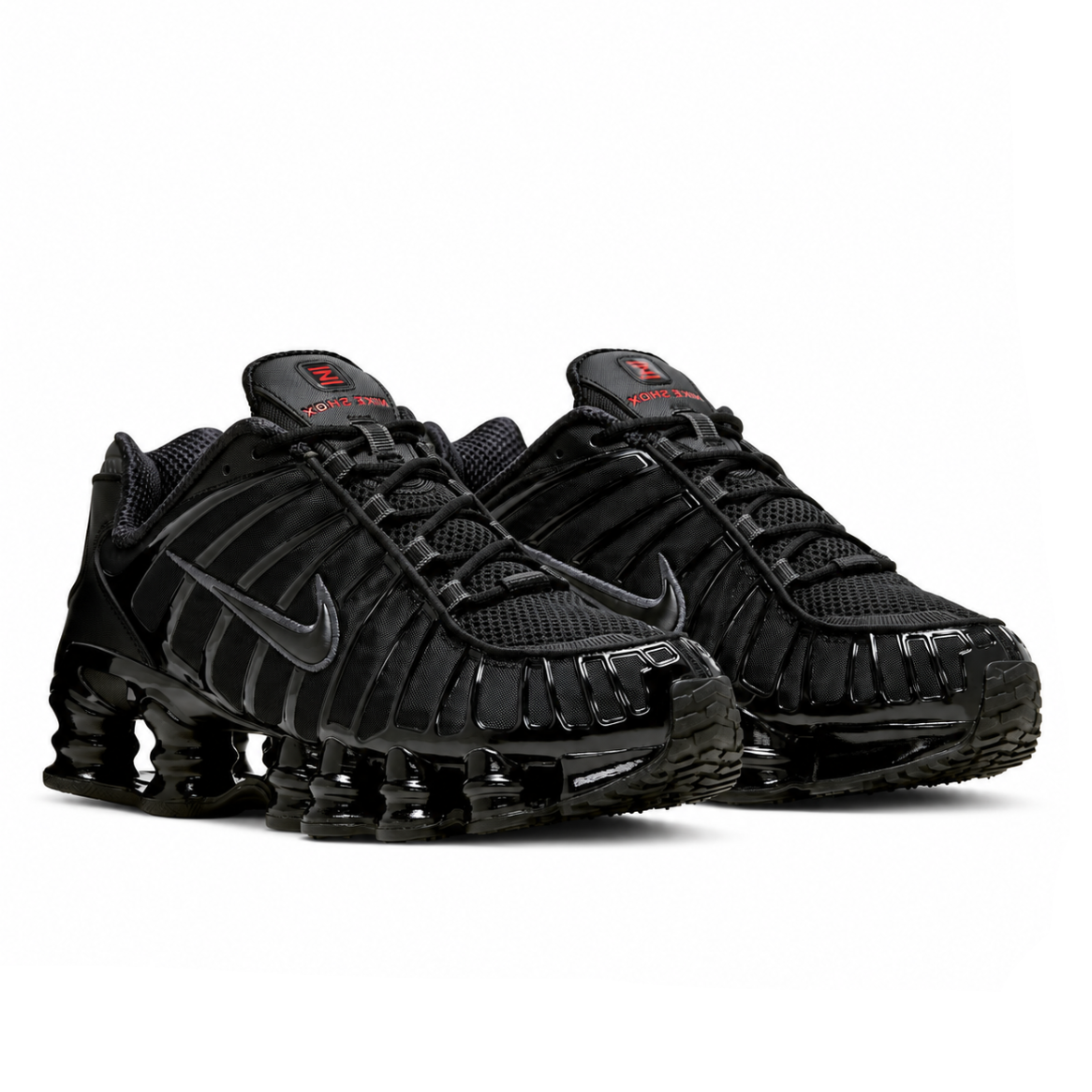 A pair of Nike Shox TL Black trainers featuring an all-black technical upper, full-length Shox cushioning columns and subtle red tongue detailing on a clean white background.