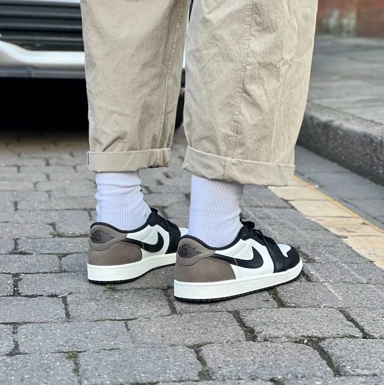 Air Jordan 1 Low OG Mocha on feet rear view with white socks and khaki trousers showing dark mocha nubuck heel, black Swoosh, and sail leather panels