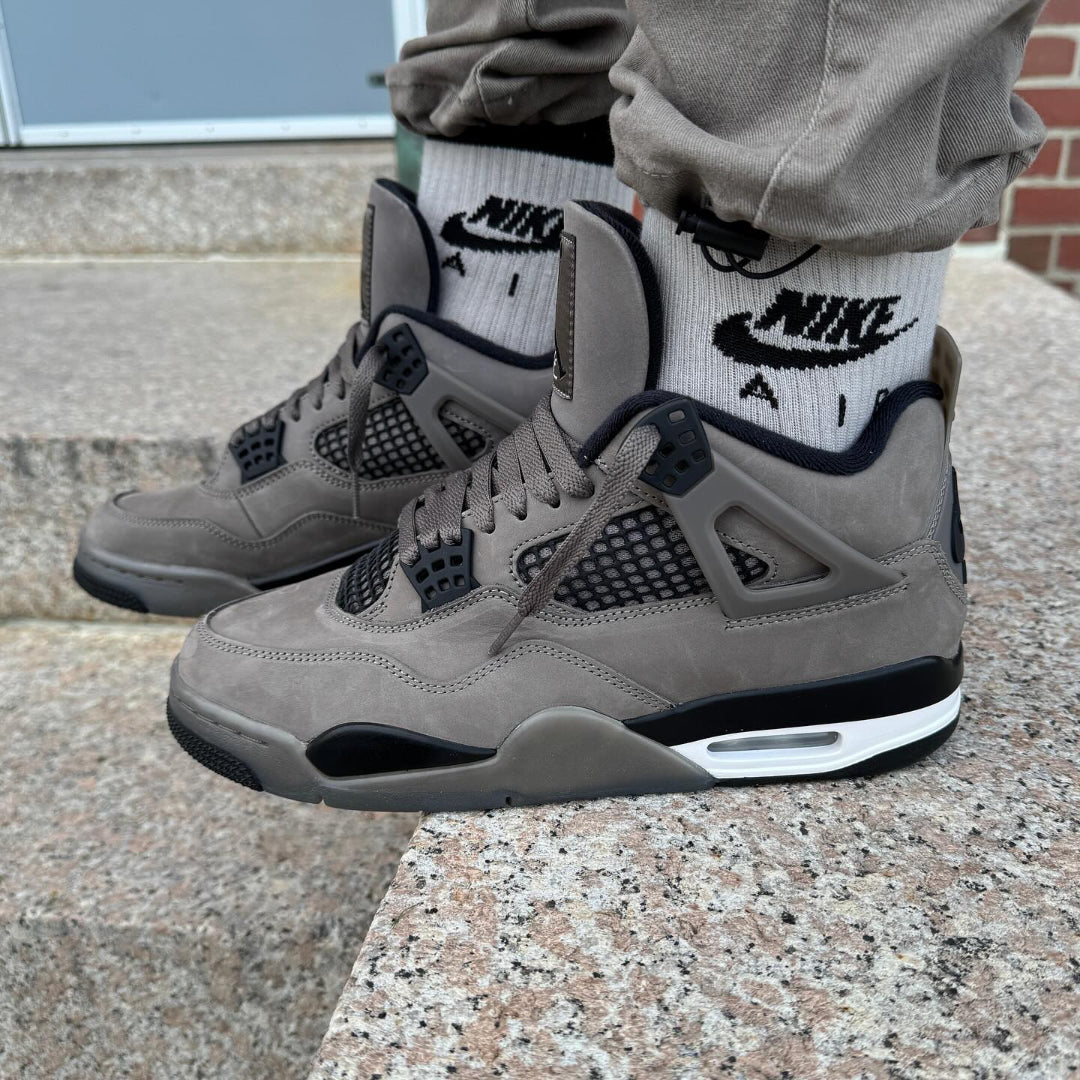 Jordan 4 Retro Cave Stone GS worn on feet with khaki joggers and Nike Air socks - front on-foot view on stone steps showing both shoes