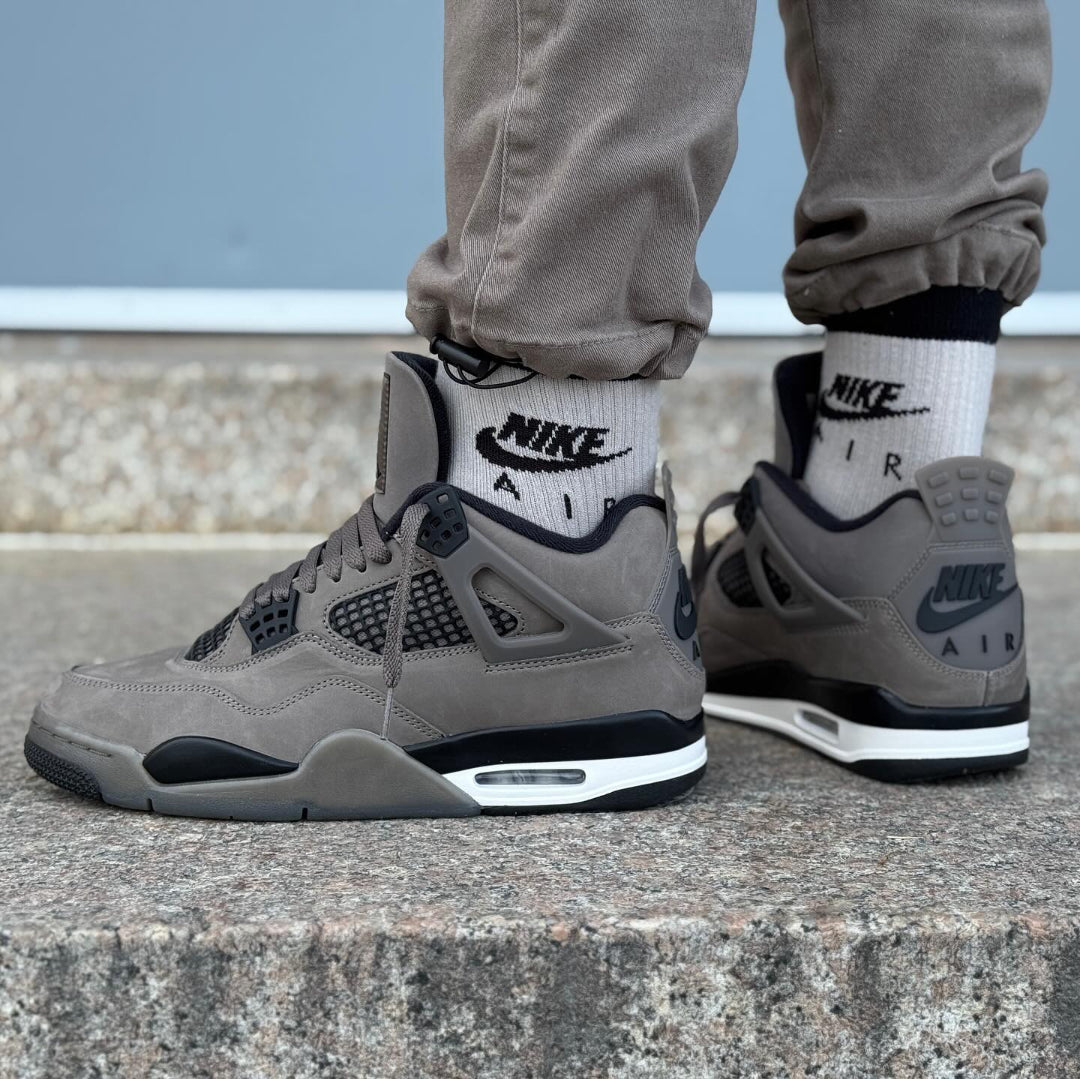 Jordan 4 Retro Cave Stone GS styled on feet with khaki trousers and Nike Air socks - side and rear on-foot view showing cave stone nubuck, black midsole and white Air unit