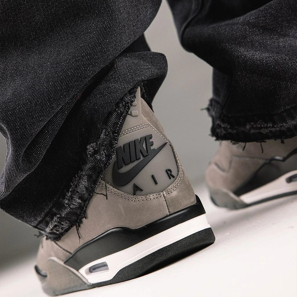 Jordan 4 Retro Cave Stone - close-up on-foot heel view with dark jeans showing embossed Nike Air branding on heel tab, cave stone nubuck and white Air-Sole midsole