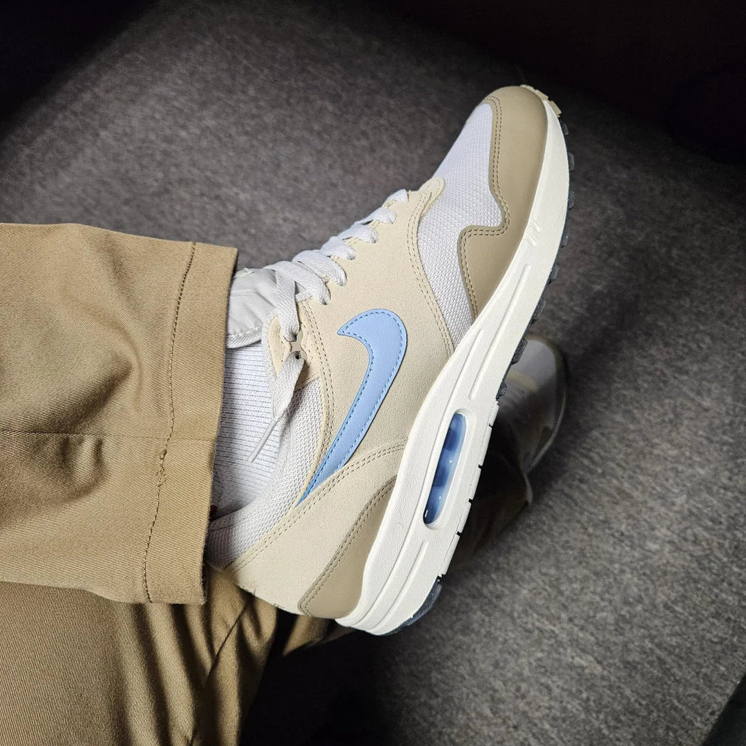 Nike Air Max 1 Light Bone Psychic Blue on foot top-down view with khaki trousers showing medial side, psychic blue Swoosh, and blue visible Air bubble