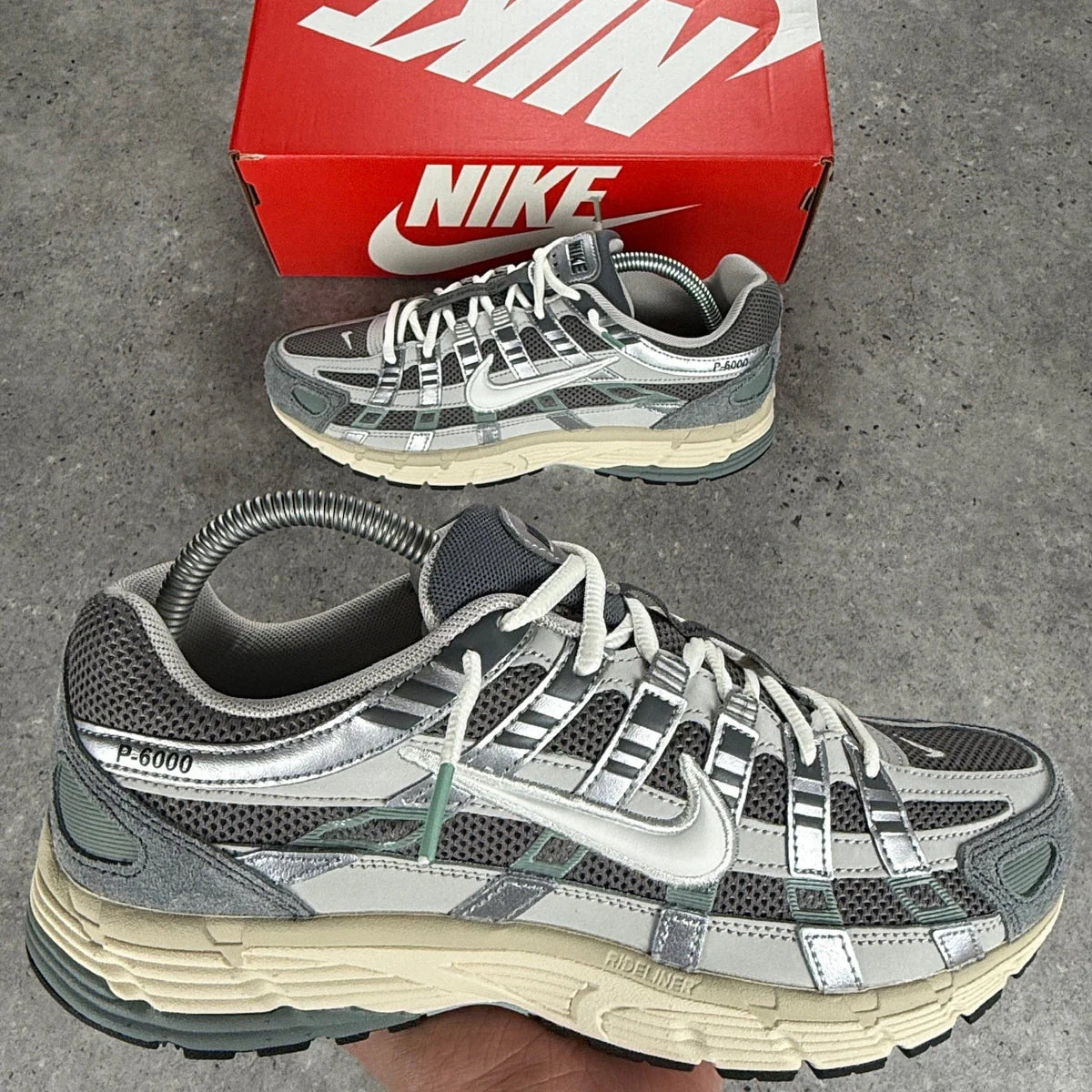 Nike P-6000 Flat Pewter on foot top-down view on stone ground showing grey suede toe, metallic overlays, white Swoosh, and P-6000 heel branding