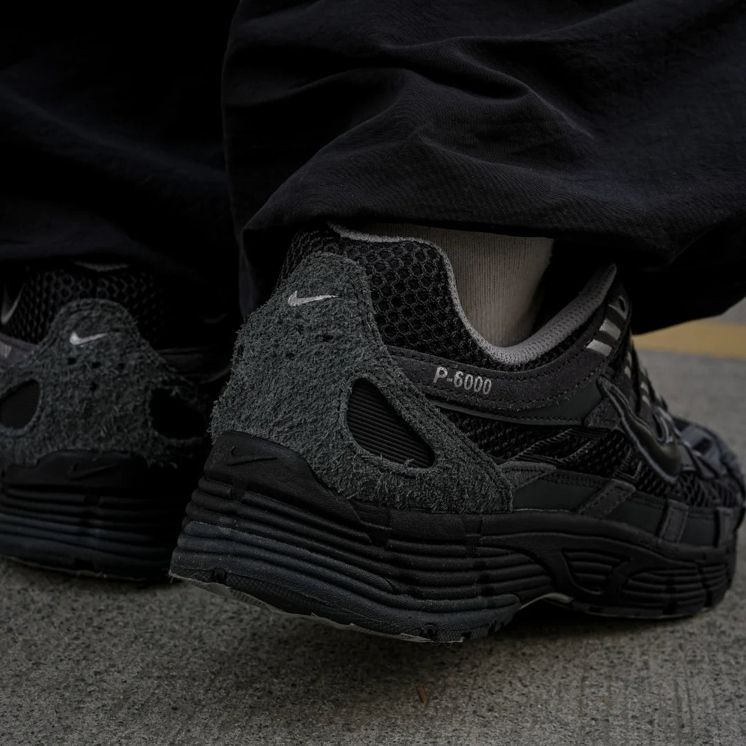 Nike P-6000 Suede Anthracite Metallic Silver on foot rear view with black trousers showing anthracite suede heel, P-6000 branding, and layered black midsole