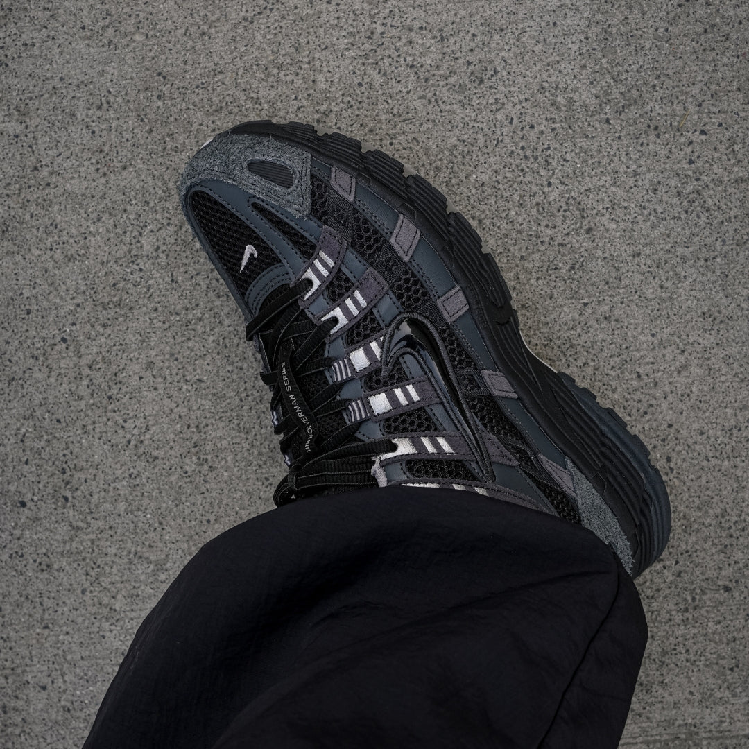 Nike P-6000 Suede Anthracite Metallic Silver top-down on foot view with black trousers showing metallic silver lace straps, black mesh upper, and Bowerman Series branding