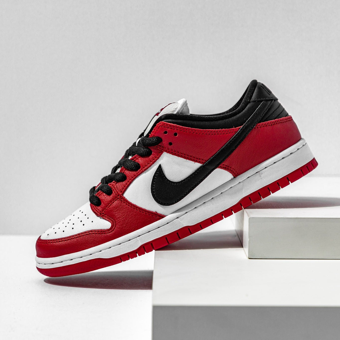 Nike SB Dunk Low J-Pack Chicago lateral side on pedestal showing red leather overlays, black Swoosh and white midsole
