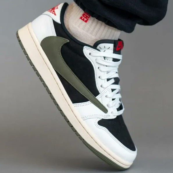Travis Scott x Air Jordan 1 Low OG Medium Olive worn on foot with black trousers and white socks - showing reverse Swoosh, olive suede panels, white leather and cream midsole