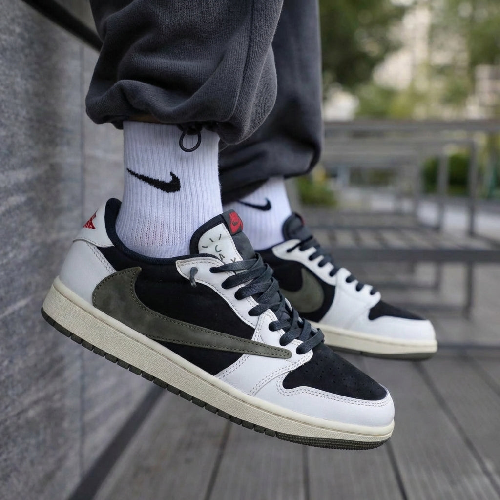 Travis Scott x Air Jordan 1 Low OG Medium Olive styled on feet outdoors with grey joggers and Nike socks - medial side showing black Swoosh, olive suede, white leather and red tongue tag