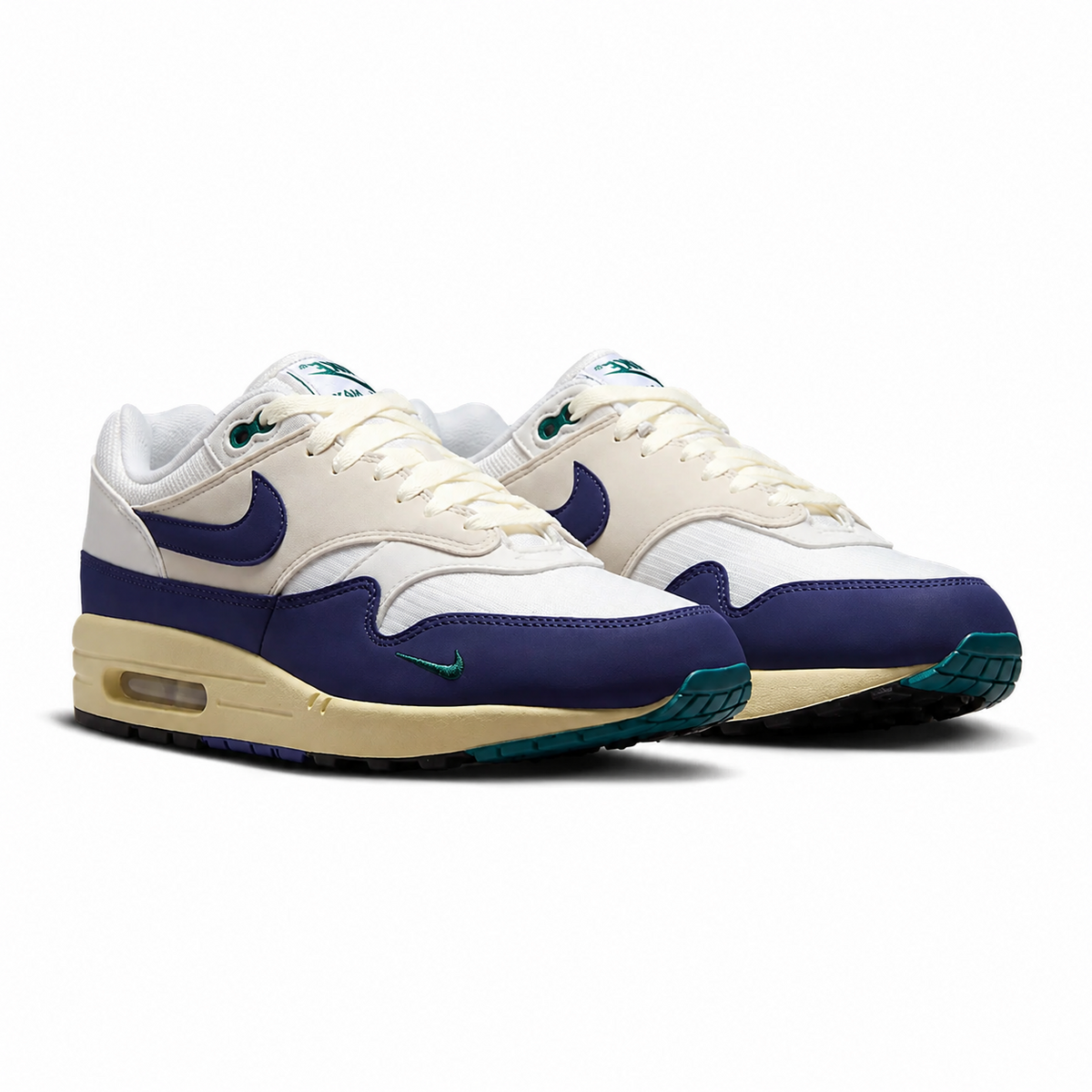 A pair of Nike Air Max 1 sneakers in a colorway of off-white, navy blue, and teal. The shoes feature off-white leather overlays, navy blue panels on the toe and Swoosh, and teal accents on the outsole and tongue.