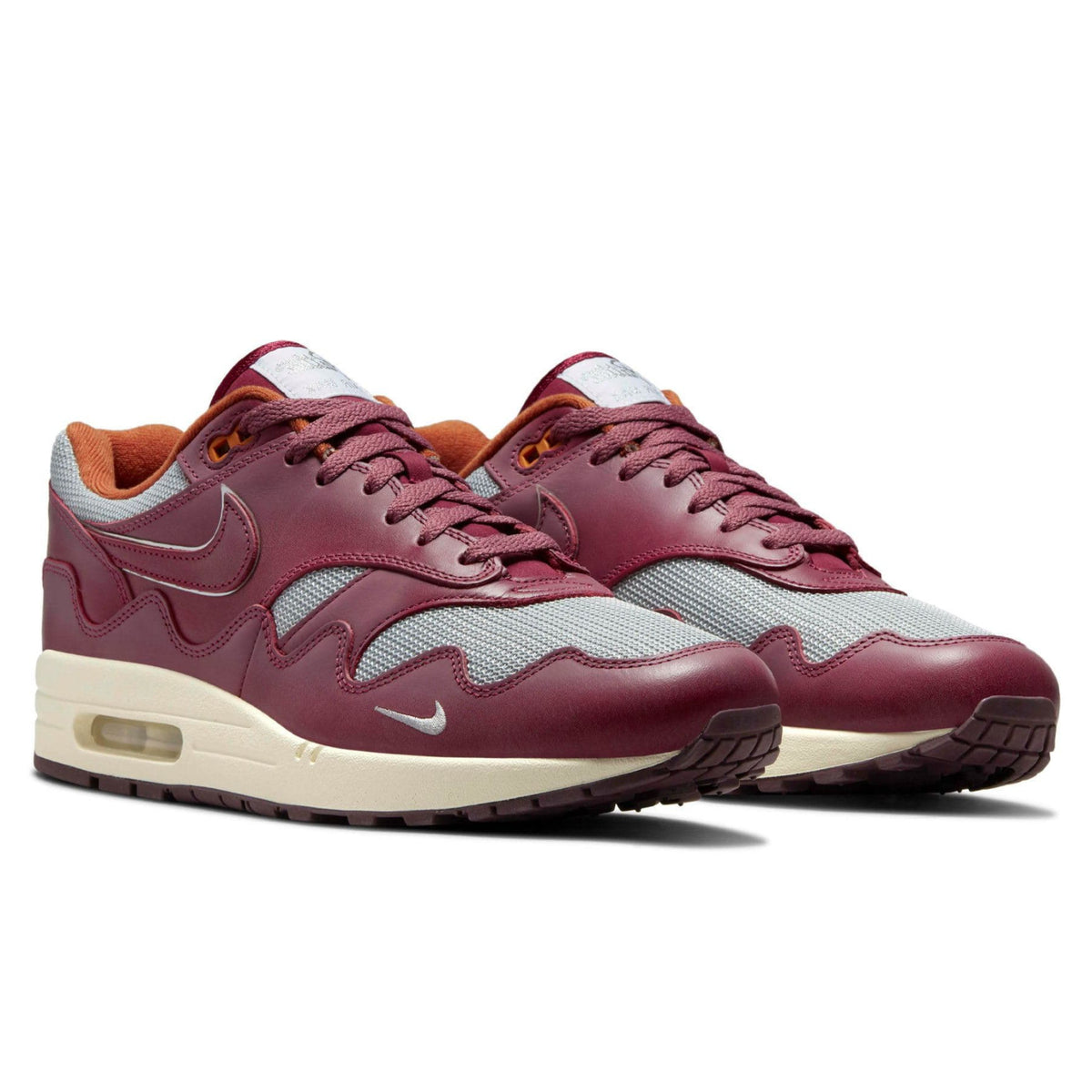 A pair of Patta x Nike Air Max 1 Night Maroon trainers featuring grey mesh, deep maroon leather overlays and signature wave-shaped mudguards on a clean white background.