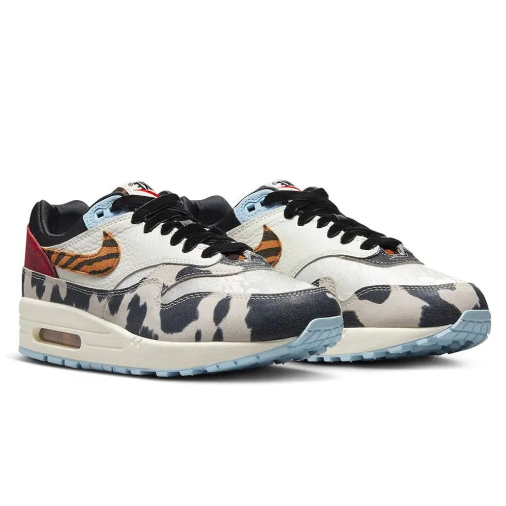 A pair of Nike Air Max 1 Wild Animal trainers featuring cow-print mudguards, tiger-striped Swooshes, paisley heel panels and light blue accents on a clean white background.