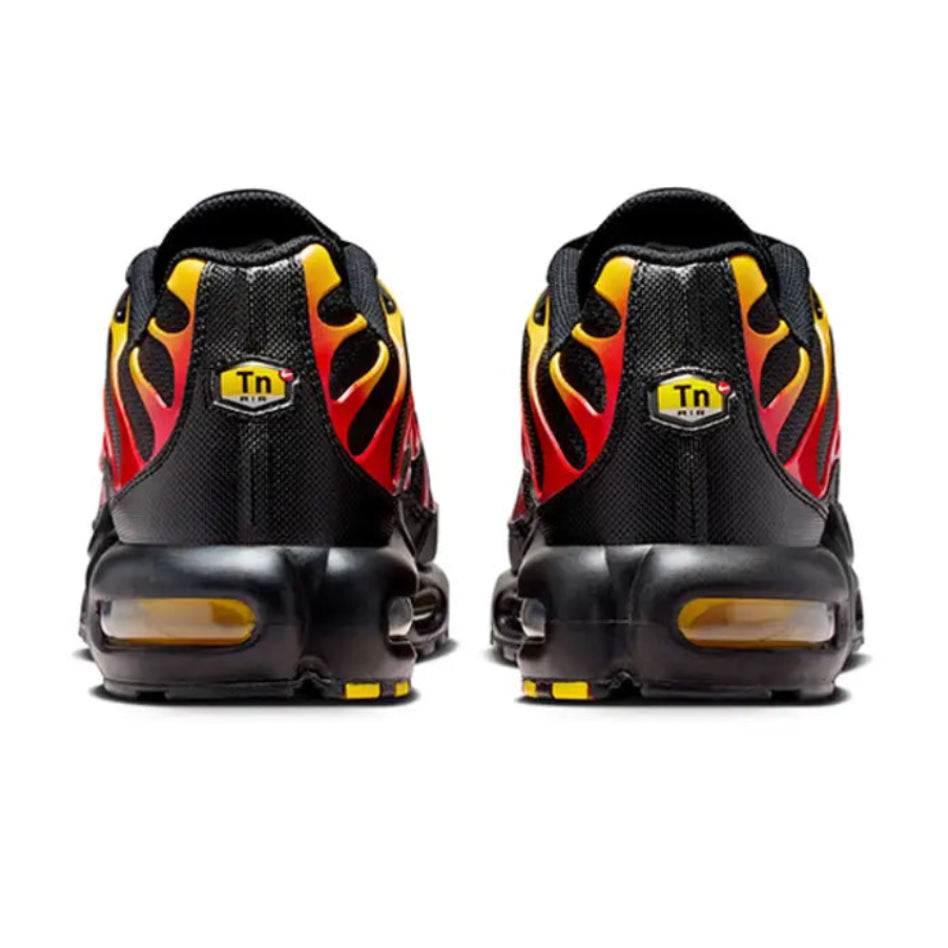 A pair of black Nike Air Max Plus sneakers shown from the back, featuring red and yellow flame graphics and a yellow 'Tn' shield logo on the heel.