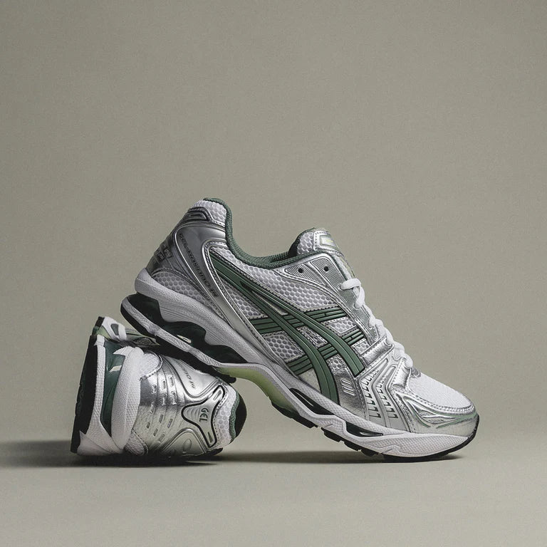 ASICS Gel-Kayano 14 White Slate Grey pair stacked on sage studio background showing white mesh upper, slate green tiger stripes, and silver metallic overlays