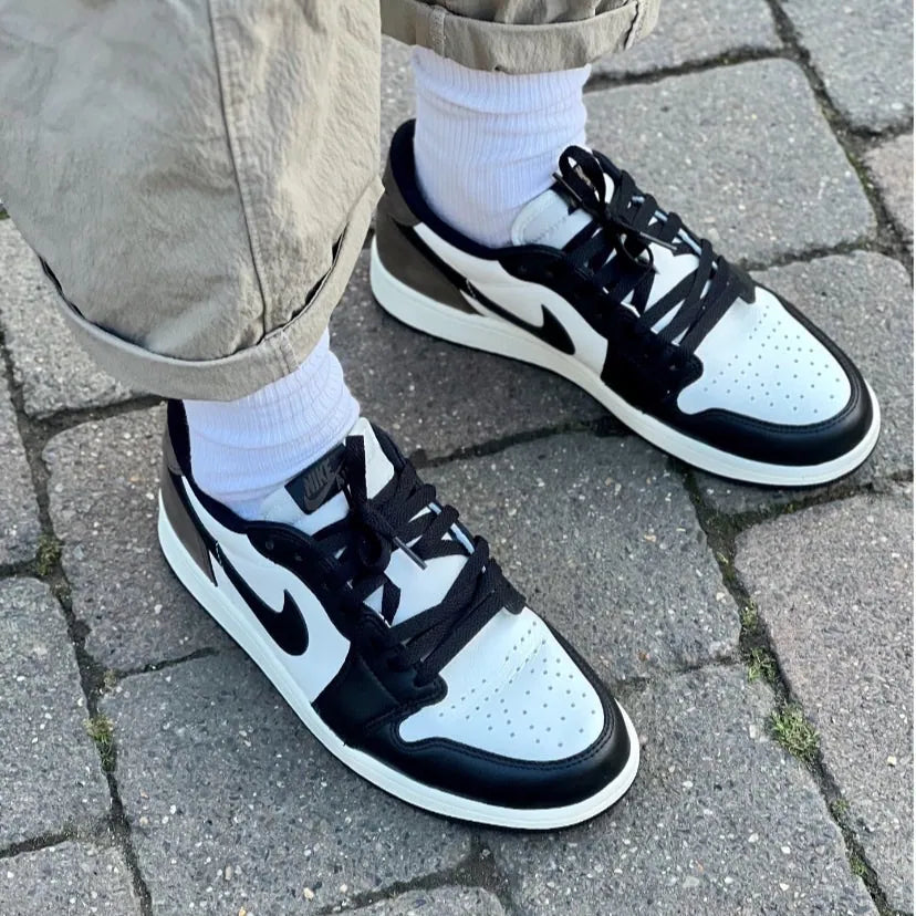 Air Jordan 1 Low OG Mocha on feet front view with white socks showing black leather toe box, sail panels, black Swoosh, and perforated toe detail
