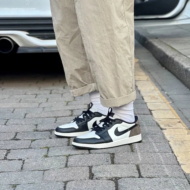 Air Jordan 1 Low OG Mocha on foot lateral view with khaki trousers showing black leather toe box, sail mid panel, black Swoosh, and mocha heel
