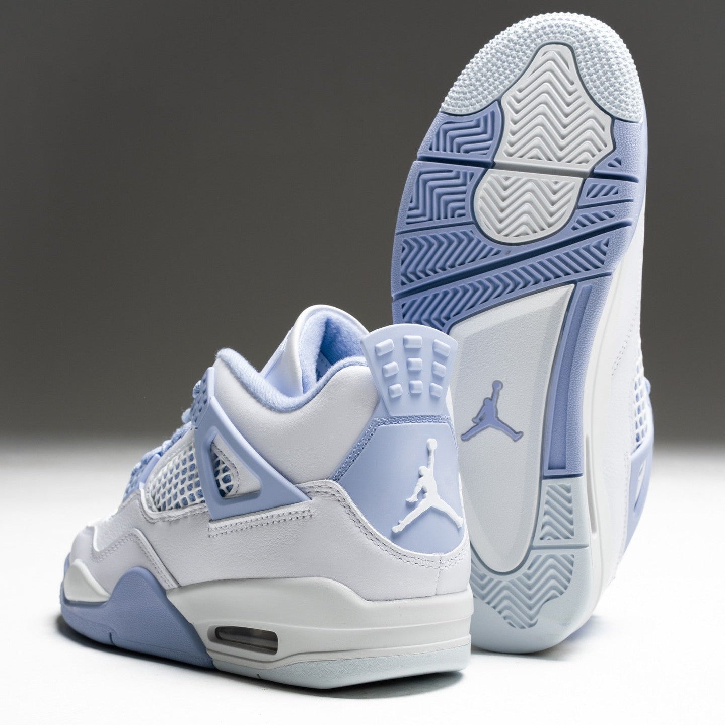 Women's Jordan 4 Retro Forget Me Not pair showing white leather upper, aluminum blue accents, Jumpman heel logo, and blue herringbone outsole