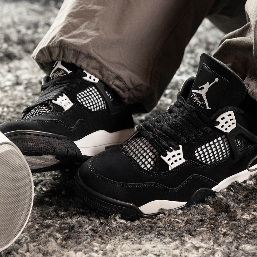 Jordan 4 Retro White Thunder on foot close-up showing black canvas upper, white eyelets, black mesh netting, white Jumpman Flight tongue, and white midsole