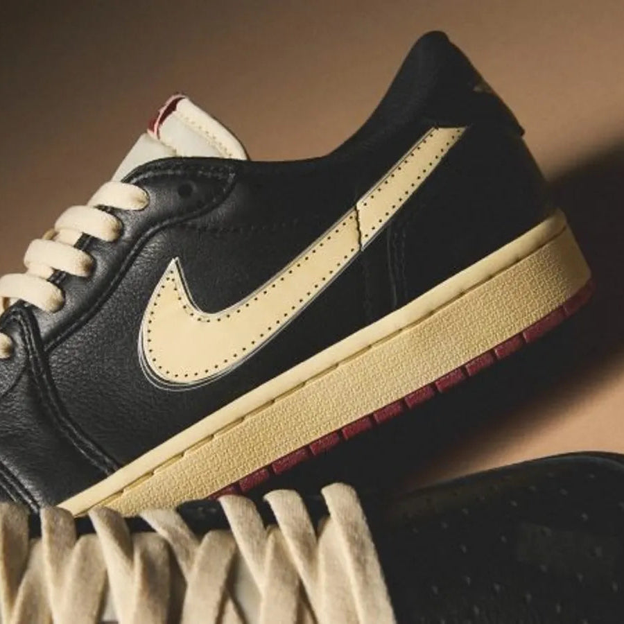 Nigel Sylvester x Jordan 1 Low OG Better With Time close-up showing muslin Swoosh on pre-distressed black tumbled leather, cream laces, aged midsole, and varsity red outsole edge