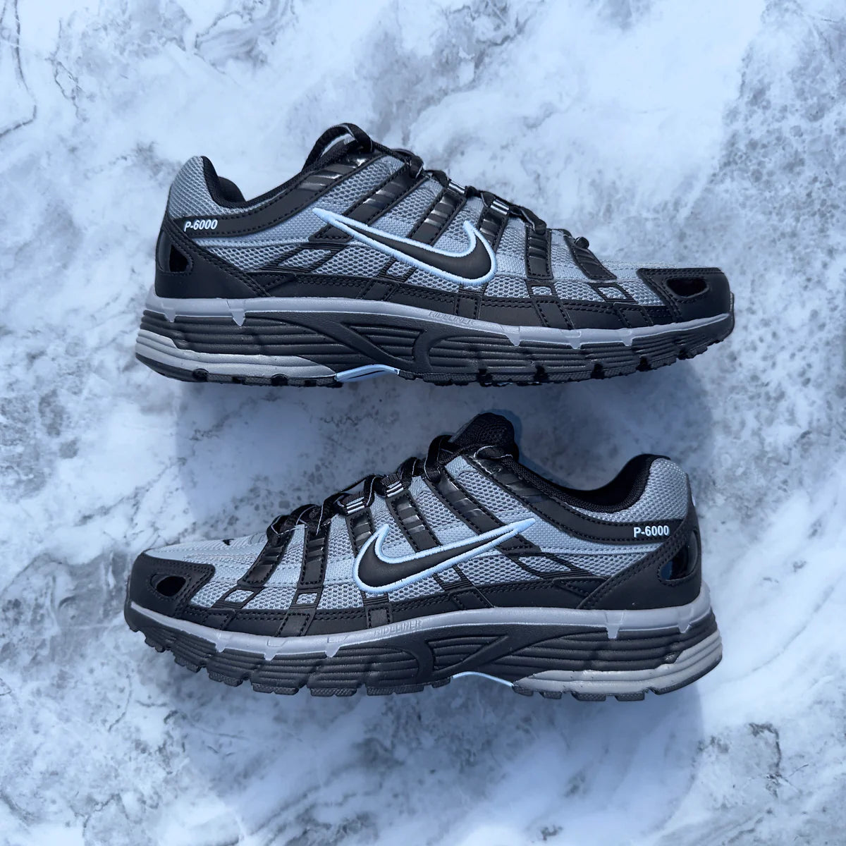 Nike P-6000 Black Cool Grey pair flat lay on marble surface showing outlined Swoosh P-6000 heel branding and grey mesh