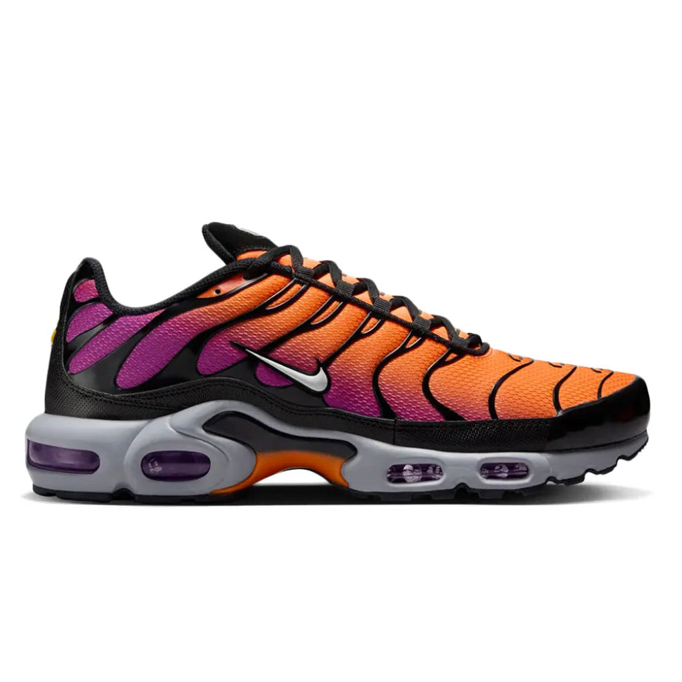 A Nike Air Max Plus sneaker shown in a side profile view on a white background. The shoe features a vibrant orange and purple gradient mesh upper, black overlays, a white Nike swoosh, and a gray and purple Air Max sole.