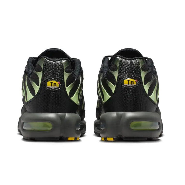 A rear view of the Nike Air Max Plus TN Iron Grey Light Liquid Lime trainers, showing the structured grey heel, bright lime detailing, TN branding and visible Air cushioning on a clean white background.
