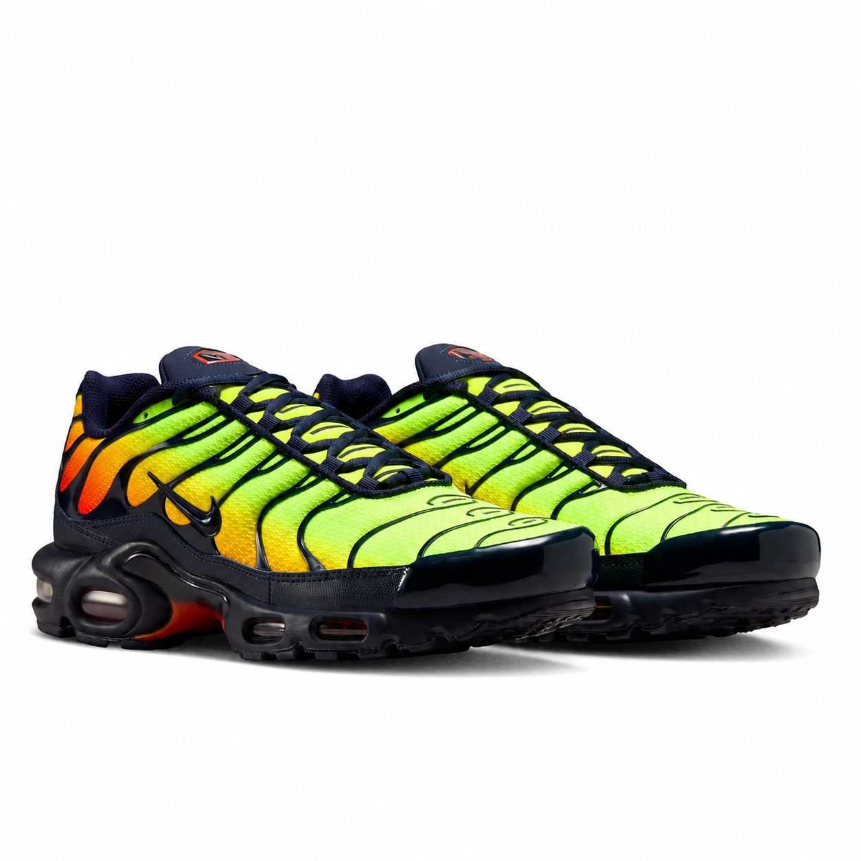 A pair of Nike Air Max Plus sneakers in a vibrant neon yellow-green, orange, and black colorway, displayed against a clean white background.