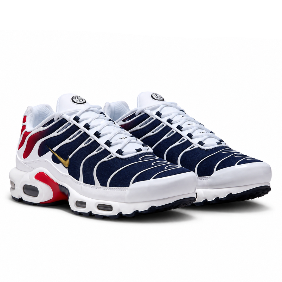 A pair of Nike Air Max Plus sneakers in navy blue, white, and red, with a gold Swoosh on the side, displayed against a clean white background.
