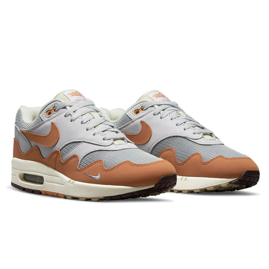A pair of Patta x Nike Air Max 1 Monarch trainers featuring Pure Platinum mesh, orange wave-shaped mudguards and visible Nike Air cushioning on a clean white background.